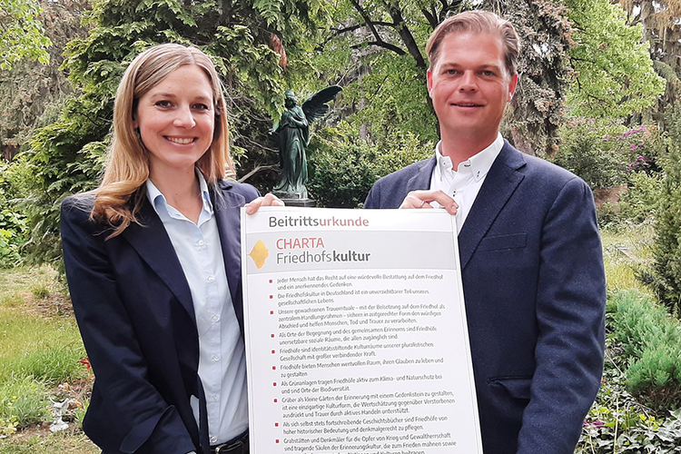 Pfarrerin Corinna Zisselsberger, Vorstandsvorsitzende, und Tillmann Wagner, Geschäftsführer des Evangelischen Friedhofsverbandes Berlin Stadtmitte präsentieren die unterzeichnete Beitrittsurkunde zur Charta Friedhofskultur (© evfbs.de)